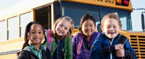 Multi-ethnic children standing in front of school bus.